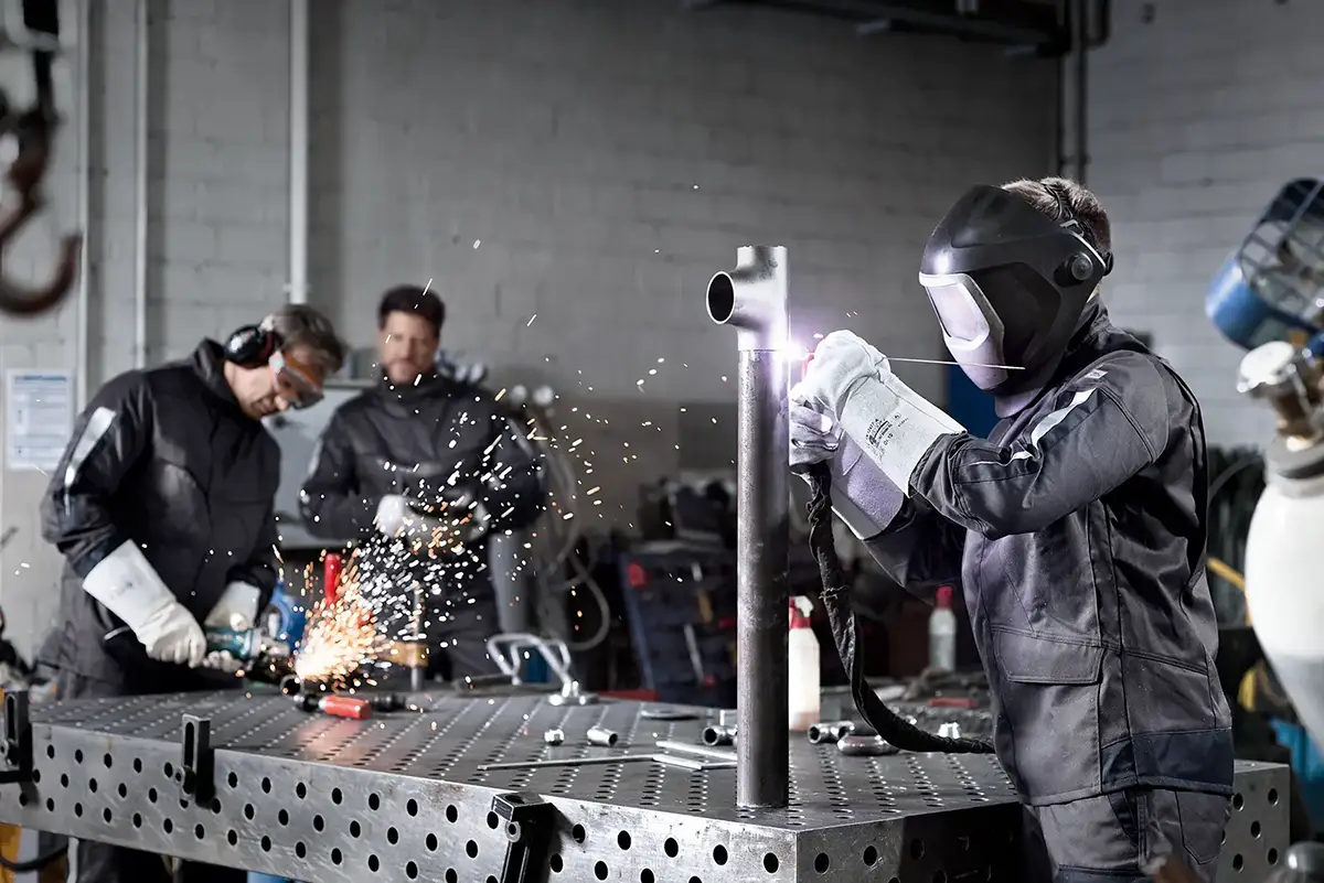 Arbeitende mit professioneller Arbeitsschutzausrüstung in einer Werkstatt bei Schweißarbeiten